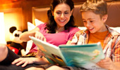 In the comfort of the Disneyland Hotel room, a boy reads a Disney storybook to his mom.