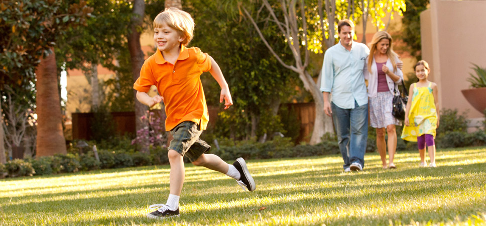 A young boy runs on the grass while his family looks on.