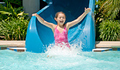 A girl, arms up and smiling, makes a small splash at the end of the water-slide ride at the Monorail Pool.