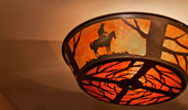 Overhead light fixture with silhouettes of tree branches and a miner on a horse.