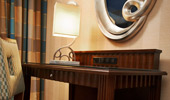 A silver bordered mirror above a dark wood desk and a Mickey-inspired reading lamp