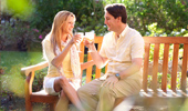 A couple sits on a bench and, in the warm glow of the California sun, raise a glass of white wine to each other.