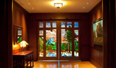 Stained glass doors at the end of the hallway show a scene with a bright blue sky, lush evergreen trees and a sparkling creek.
