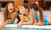 3 girls stretch out be the edge of the pool and laugh.