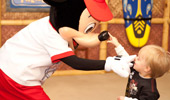 A toddler touches the tip of Mickey's nose; Mickey touches the toddler's nose.