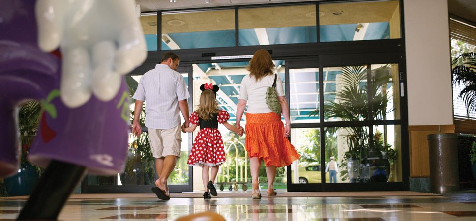 A mom and dad hold hands with their young girl who is dressed as Minnie Mouse.
