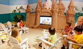 Kids sit in a circle of chairs around the sandcastle themed TV at the Paradise Theater.