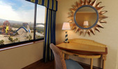 A yellow computer table beneath a mirror in a sun-shaped frame sit near a large window with a Theme Park view.